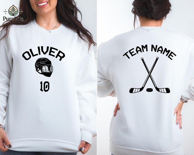 May include: White sweatshirt with black text and graphic. The front of the sweatshirt says "OLIVER" with a hockey helmet graphic and the number "10". The back of the sweatshirt says "TEAM NAME" with two hockey sticks crossed over each other.