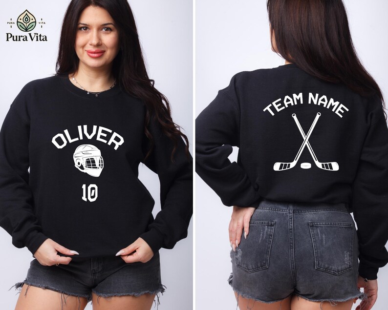 May include: Black sweatshirt with white text and graphic. The text on the front says "Oliver" and has a hockey helmet graphic with the number "10" below it. The back of the sweatshirt says "Team Name" with two crossed hockey sticks and a puck.