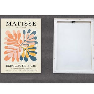 May include: A white canvas print with a colorful abstract design by Henri Matisse. The design features a stylized floral motif in shades of pink, yellow, blue, and green. The text "MATISSE THE CUT-OUTS BERGGRUEN & CIE 70 RUE DE L'UNIVERSITE, PARIS-VIH "My curves are not crazy" Henri Matisse, Jazz, 1947" is printed below the design.