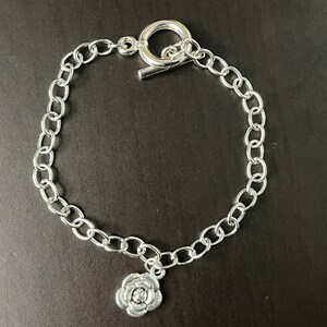 May include: A silver chain bracelet with a silver rose charm. The bracelet has a lobster clasp.
