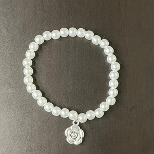 May include: A white pearl bracelet with a silver rose charm.