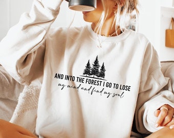 May include: A white sweatshirt with a black graphic of trees and the text "AND INTO THE FOREST I GO TO LOSE my mind and find my soul".