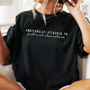 May include: A black t-shirt with the text "Emotionally attached to fictional characters" in white lettering.