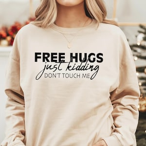 May include: A beige sweatshirt with the text "FREE HUGS just kidding DON'T TOUCH ME" printed in black.