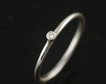 Op de afbeelding: Een eenvoudige zilveren ring met een enkele, kleine, heldere diamant in het midden.
