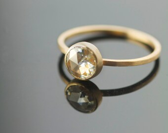 Puede incluir: Un anillo de oro con una piedra preciosa redonda y facetada, transparente. El anillo es simple y elegante.