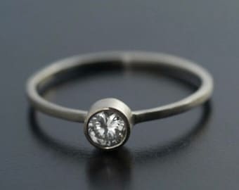 May include: A simple silver band ring with a single round clear gemstone set in a bezel setting.