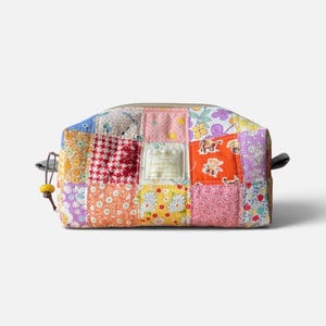 Peut inclure: Une trousse zippée rectangulaire présentant un motif patchwork coloré avec divers imprimés floraux, géométriques et animaliers dans des tons de rose, orange, jaune et violet. Une petite étiquette en tissu porte l'inscription It's Lovely Day.