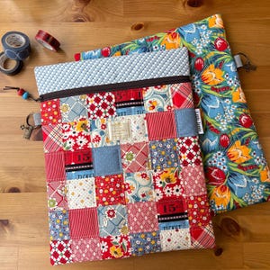 May include: A patchwork fabric zippered pouch with a variety of red, white, and blue patterns. A second pouch with a floral pattern is next to it. Decorative tape rolls are in the upper left corner.