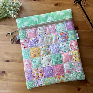 May include: A patchwork zippered pouch with a variety of floral patterns in pastel colors. The top section is light green with white daisy print. The pouch has a brown zipper and a small tag that says "Little Jamie".