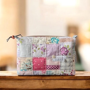 May include: A patchwork fabric cosmetic bag with a zipper closure. The bag features a variety of floral and polka dot patterns in pastel colors. The bag has a small tag that says "fait à la main" and a star.