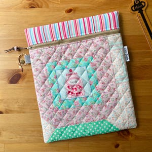 May include: A quilted zipped pouch featuring a central square with a candy jar graphic labelled Candy, surrounded by pink floral, teal polka dot, and striped fabric panels. A metal zip pull with a small charm is attached to the side.