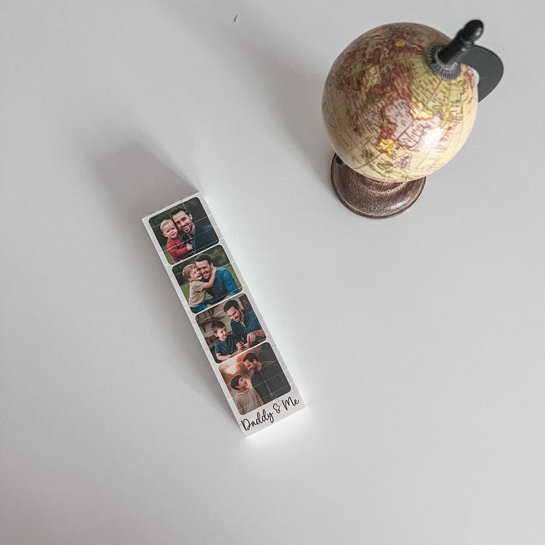 May include: A white bookmark with four family photos and the text "Daddy & Me." A small globe with a brown base sits nearby. The bookmark is rectangular and features a series of family photos.