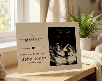 Może przedstawiać: Kremowa ramka na zdjęcia z napisem "hi grandma" i "I can't wait to meet you! Baby Jones September 2023." Ramka zawiera obraz USG i jest ustawiona na drewnianej powierzchni.
