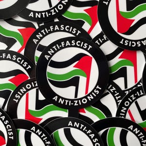 Peut inclure: Plusieurs autocollants ronds avec un bord noir. Chaque autocollant présente un motif avec un drapeau rouge, des rayures vertes et noires, et les mots "ANTI-FASCISTE" et "ANTI-ZIONISTE" en cercle.