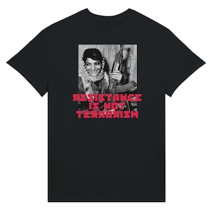 May include: A black short-sleeved t-shirt featuring a central black and white photographic print of a smiling individual wearing a keffiyeh and holding a rifle. Below the image, the text RESISTANCE IS NOT TERRORISM is printed in bold red letters.