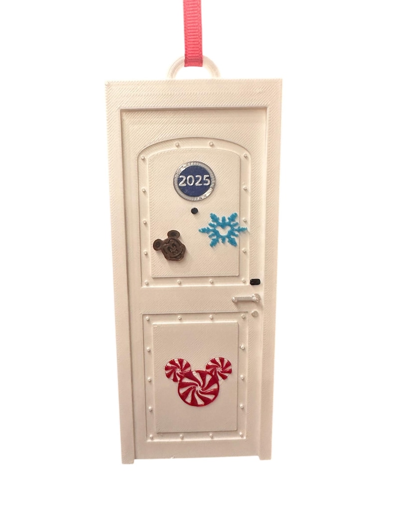May include: White rectangular ornament with a door design. Features a Mickey Mouse head made of candy canes, a snowflake, and a Mickey Mouse head. The year 2025 is displayed on the top panel. A pink ribbon is attached for hanging.