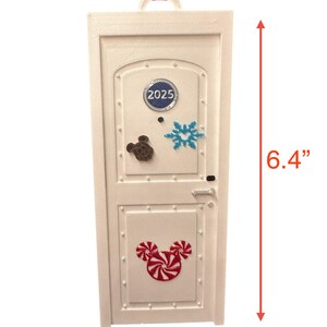 May include: White door-shaped ornament with a pink ribbon for hanging. The ornament features a Mickey Mouse head made of candy canes, a snowflake, and the year 2025. It measures 6.4 inches tall and 2.6 inches wide.