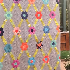 May include: A quilt with a gray background and a pattern of colorful flowers. The quilt is hanging on a wall and the text "Garden Party" is visible at the top of the quilt.