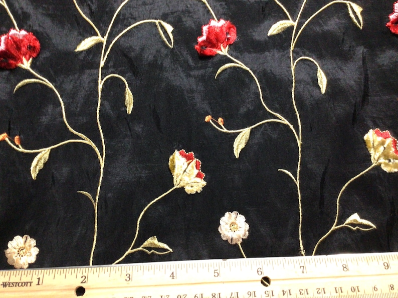 May include: Black fabric with an embroidered floral pattern in red, gold, and white. The fabric is shown with a ruler for scale.