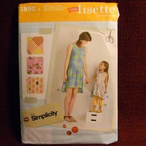 May include: A sewing pattern for a dress for a child, with a blue and white patterned dress and a pink and white patterned dress. The pattern is from Simplicity and is called "Little Lisette".