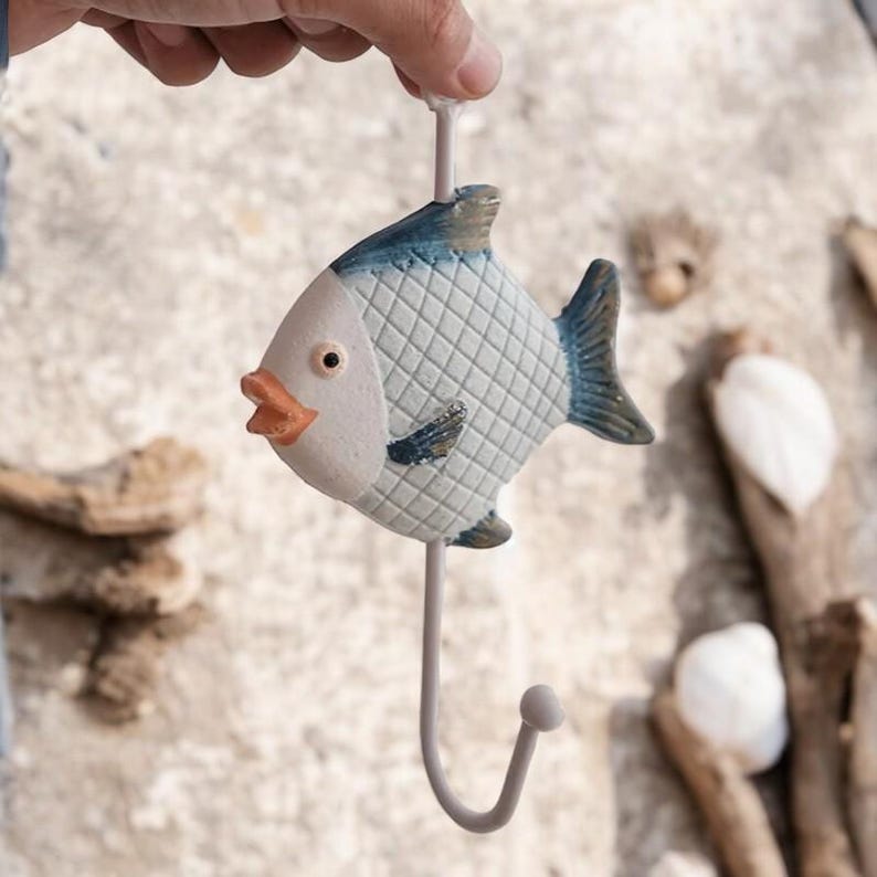 May include: A white and blue ceramic fish hook with a metal hook. The fish has a checkered pattern and a small orange mouth.