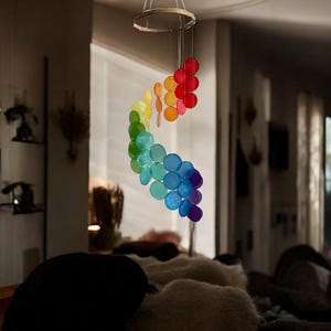 Può includere: Un mobile arcobaleno fatto di dischi rotondi in plastica traslucida appesi a un anello di legno. I dischi sono disposti a spirale, con i colori che passano dal rosso all'arancione, al giallo, al verde, al blu e al viola.