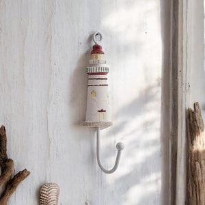 May include: White lighthouse shaped hook with a red roof and a metal hook. The hook is mounted on a white wall.