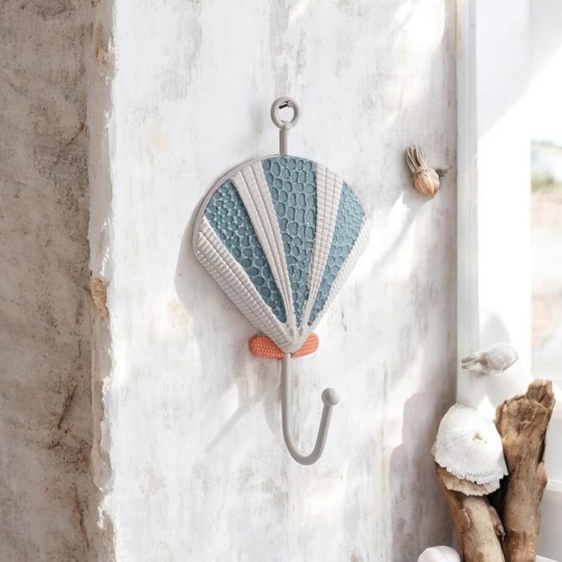 May include: A blue and white seashell shaped wall hook with a metal hook. The hook is attached to the wall with a screw.