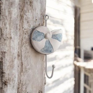May include: A white and blue seashell-shaped hook with a metal hook. The hook is mounted on a wooden wall.