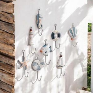 Peut inclure: Un ensemble de huit crochets muraux décoratifs sur le thème nautique. Les crochets sont en métal et ont une finition blanche. Les crochets sont décorés de différentes créatures marines, dont un hippocampe, un poisson, une étoile de mer et un voilier. Les crochets sont également décorés d'un phare, d'une bouée de sauvetage et d'une montgolfière.