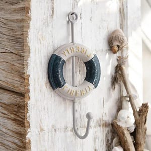 May include: A white and blue life preserver shaped hook with the word "LIBERTY" written on it. The hook is attached to a white wooden wall.