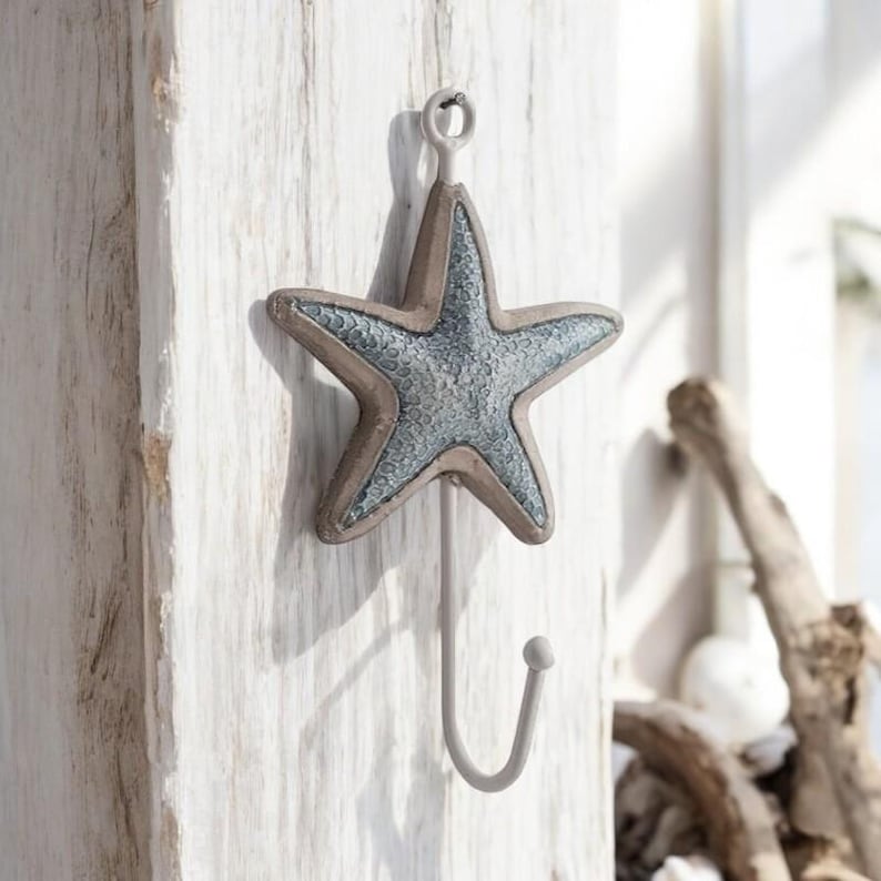 May include: A white metal hook with a blue and brown starfish design. The hook is mounted on a white wooden surface.