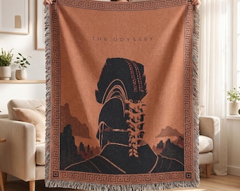 May include: A woven throw blanket in a terracotta orange hue featuring a dark navy blue graphic of a helmeted figure and the text THE ODYSSEY. The design is framed by a black Greek key border and finished with a fringed edge on the top and bottom.