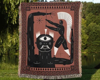 May include: A rectangular woven throw blanket featuring a terracotta background with a black and white graphic illustration of a warrior figure with a spear standing on a large cyclops head, framed by a black Greek key border with fringed edges.