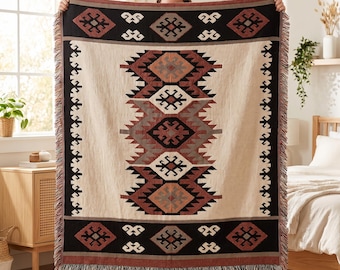 May include: A rectangular woven throw blanket featuring a central vertical column of geometric diamond patterns in shades of rust, black, and cream. The blanket has a wide black border with repeating diamond motifs and a fringed edge on the bottom.