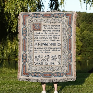 May include: A woven throw blanket featuring a decorative border with blue and red knotwork and green vines. The centre displays black text that reads: Because how could the end be happy? EVEN DARKNESS MUST PASS. THERE'S SOME GOOD IN THIS WORLD.
