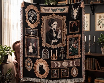 May include: A black woven throw blanket featuring a collage of gothic-inspired illustrations in ornate gold frames, including a skeleton in Victorian attire, a black cat, moon phases, a skull, keys, candles, and various botanical elements.