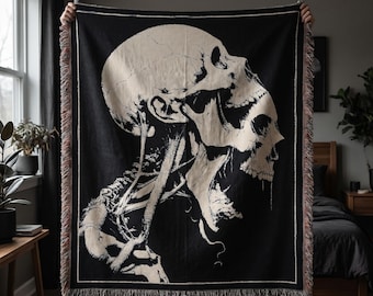 May include: A rectangular woven throw blanket featuring a large, high-contrast cream-colored graphic of a human skull and upper spine set against a solid black background. The blanket has a decorative fringed edge along all four sides.