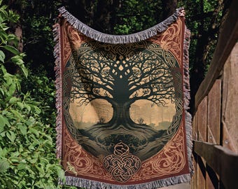 May include: A woven throw blanket featuring a large, dark tree silhouette centered within a circular frame, surrounded by intricate Celtic knotwork patterns in shades of deep red, brown, and gold, finished with a fringed edge on all sides.