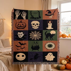 May include: A woven throw blanket featuring a grid of Halloween-themed illustrations including skeleton hands, a tombstone with RIP text, a witch hat, a jack-o'-lantern, a skull, a candle, a vampire, a spider web, a black cat, bats, a cauldron, an eye, a ghost, and a witch.