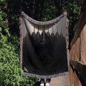 May include: A black and white woven tapestry featuring a design of hooded figures holding swords. The tapestry is draped over a wooden bridge.