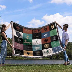 Lord of the Rings Fantasy emblems throw blanket held by pair outdoors, woven patchwork design with magical symbols, decorative fringe by lakeside