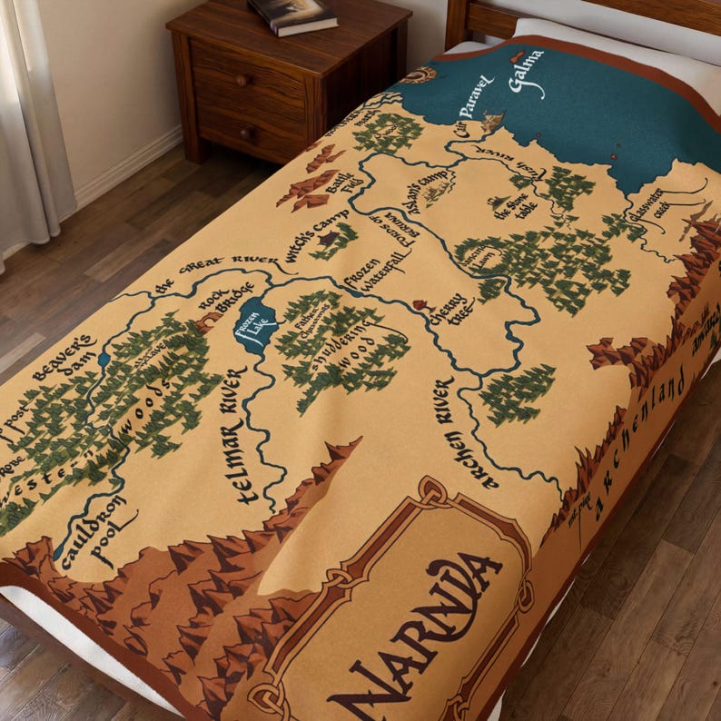 May include: A tan throw blanket featuring a map of Narnia with brown, green, and blue accents. The map includes place names like Telmar River, Witch's Camp, and Paravel. The word "Narnia" is prominently displayed.
