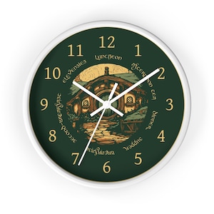 May include: A round wall clock with a white frame and a dark green face. The clock features gold numbers 1 through 12, white hands, and a central illustration of a round-door house. Text around the center reads: Breakfast, Second-Breakfast, Elevensies, Luncheon, Afternoon Tea, Dinner, Supper.