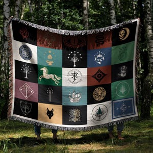 Magical patchwork blanket displayed in forest setting, woven throw with Lord of the rings flags and symbols, colorful squares with fantasy emblems and fringe trim