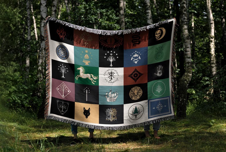 Magical patchwork blanket displayed in forest setting, woven throw with Lord of the rings flags and symbols, colorful squares with fantasy emblems and fringe trim