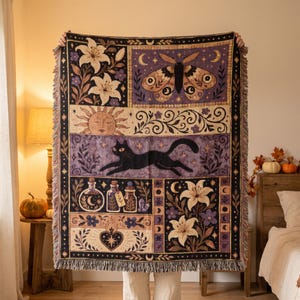 May include: A woven throw blanket featuring a multi-panel design with a black cat, a large moth, white lilies, a sun face, and potion bottles. The color palette includes shades of purple, black, cream, and gold with a fringed edge finish.