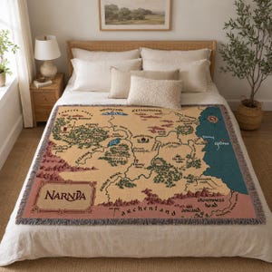 May include: A woven throw blanket featuring a map of Narnia in shades of tan, green, and blue. The blanket has a fringed edge and the word "NARNIA" is displayed in a decorative font.