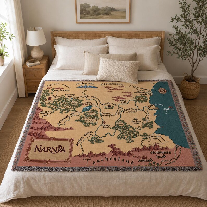 May include: A woven throw blanket featuring a map of Narnia in shades of tan, green, and blue. The blanket has a fringed edge and the word "NARNIA" is displayed in a decorative font.